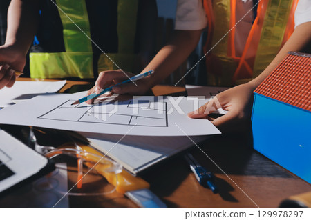 Closeup of team of industrial engineers meeting analyze machinery blueprints consult project on table in manufacturing factory. Working in manufacturing plant or production plant. Closeup of team of industrial engineers meeting analyze machinery blueprints consult project on table in manufacturing factory. Working in manufacturing plant or production plant. 129978297