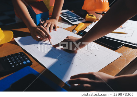 Closeup of team of industrial engineers meeting analyze machinery blueprints consult project on table in manufacturing factory. Working in manufacturing plant or production plant. Closeup of team of industrial engineers meeting analyze machinery blueprints consult project on table in manufacturing factory. Working in manufacturing plant or production plant. 129978305