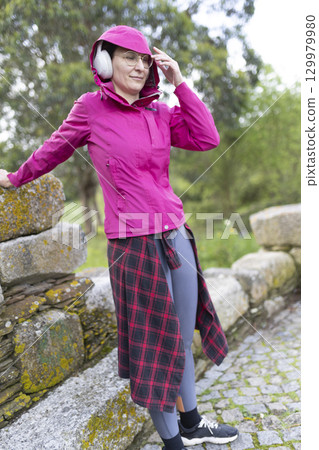 Woman wearing headphones listening to music while relaxing in park 129979980