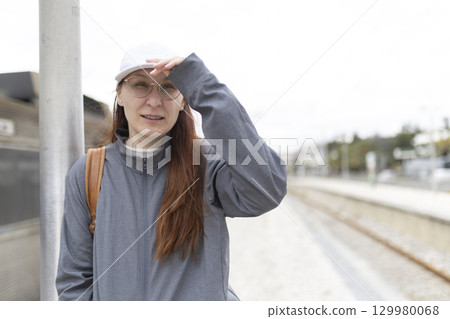 Tourist looking for train at station covering eyes from sunlight 129980068