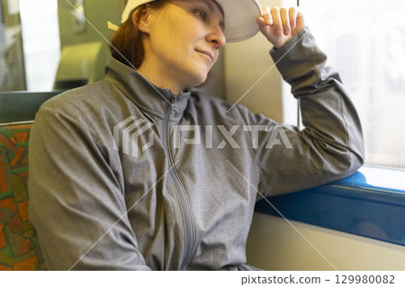 Woman wearing white cap traveling by train and looking out the window 129980082