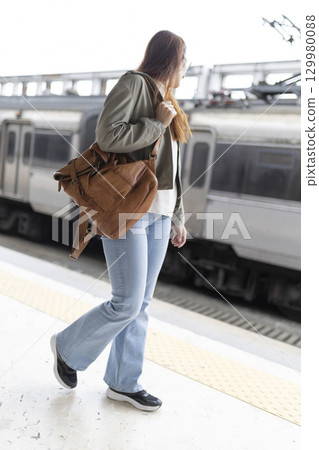 Young woman walking on train station platform with leather bag 129980088