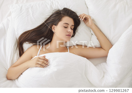Peaceful Caucasian woman sleeping comfortably in bed with soft pillow and blanket early in morning. 129981267
