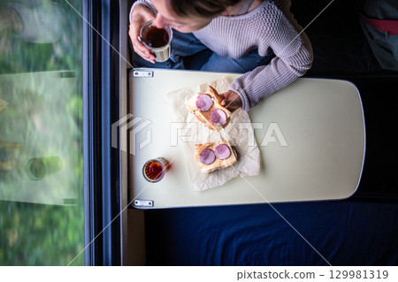 Solo travel in train. Calm woman eat sausage sandwich drink tea in long distance train wait neighbor Solo travel in train. Calm woman eat sausage sandwich drink tea in long distance train wait neighbor 129981319