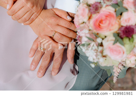 Close-up image of hands wearing wedding rings, symbolizing love and commitment. A beautifully arranged bouquet accompanies the scene, enhancing the joyful and romantic atmosphere Close-up image of hands wearing wedding rings, symbolizing love and commitment. A beautifully arranged bouquet accompanies the scene, enhancing the joyful and romantic atmosphere 129981981