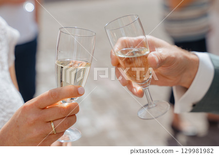 Two people clinking champagne glasses in a celebratory toast. The atmosphere suggests a joyous occasion, possibly a wedding or special event, marked by shared happiness and connection Two people clinking champagne glasses in a celebratory toast. The atmosphere suggests a joyous occasion, possibly a wedding or special event, marked by shared happiness and connection 129981982