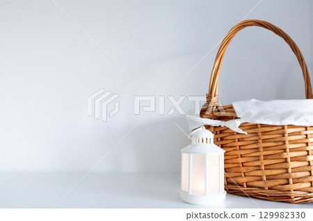 Wicker basket with white lantern on minimalist surface 129982330
