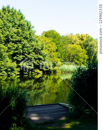 Tranquil lake scene with lush trees and wooden dock in summer Tranquil lake scene with lush trees and wooden dock in summer 129982338
