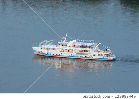 A pleasure boat sails along the River. Pleasure boat cruises along the tranquil waters of the Yenisei River showcasing scenic beauty during a summer day A pleasure boat sails along the River. Pleasure boat cruises along the tranquil waters of the Yenisei River showcasing scenic beauty during a summer day 129982449