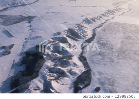 Aerial view shows a vast, pristine snowcovered landscape with hills and a winding river. Mountainous hilly snow-covered ridge imho aerial view. Minino, Krasnoyarsk Aerial view shows a vast, pristine snowcovered landscape with hills and a winding river. Mountainous hilly snow-covered ridge imho aerial view. Minino, Krasnoyarsk 129982503