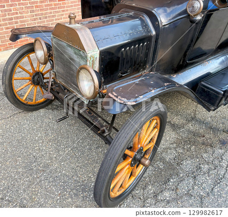 Vintage Ford Model T Car With Orange Wheels Parked Near a Brick Wall 129982617