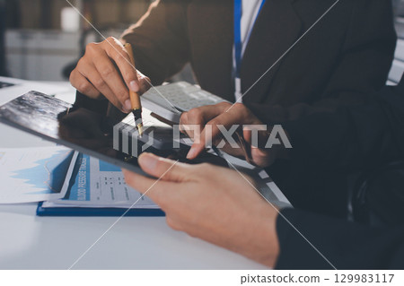 Focused young businessman signing agreement with skilled lawyer in eyeglasses. Concentrated financial advisor showing place for signature on paper contract document to male client at meeting in office 129983117