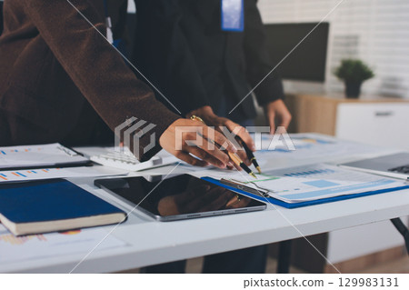Focused young businessman signing agreement with skilled lawyer in eyeglasses. Concentrated financial advisor showing place for signature on paper contract document to male client at meeting in office 129983131