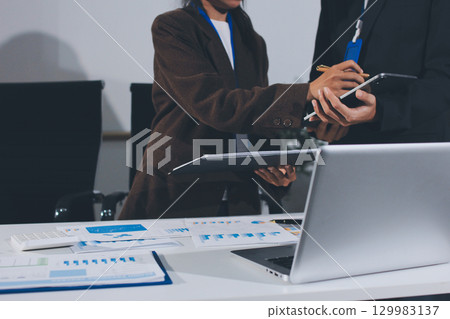 Focused young businessman signing agreement with skilled lawyer in eyeglasses. Concentrated financial advisor showing place for signature on paper contract document to male client at meeting in office 129983137