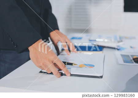 Focused young businessman signing agreement with skilled lawyer in eyeglasses. Concentrated financial advisor showing place for signature on paper contract document to male client at meeting in office 129983160