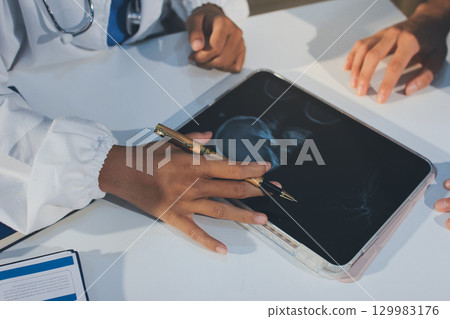 Cropped shot of an unrecognisable doctor sitting with his patient and showing her x-rays on a digital tablet 129983176