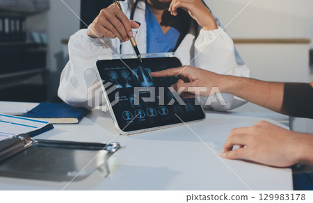 Cropped shot of an unrecognisable doctor sitting with his patient and showing her x-rays on a digital tablet 129983178
