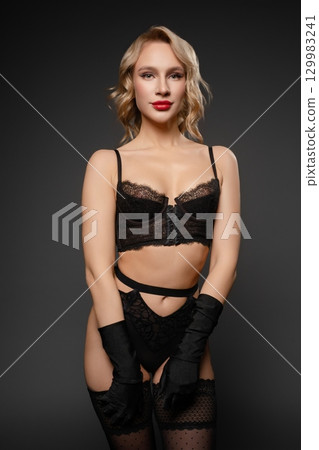 Sensual woman in elegant lingerie poses confidently against a dark backdrop 129983241