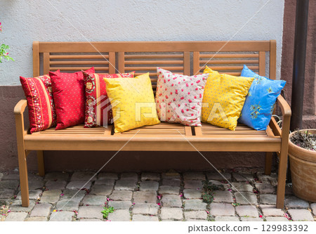 Wood romantic bench with a lot of multicolor pillows outdoor near stone house. Wood romantic bench with a lot of multicolor pillows outdoor near stone house. 129983392