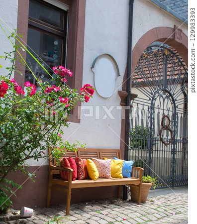Wood romantic bench with a lot of multicolor pillows outdoor near stone house and rose. Wood romantic bench with a lot of multicolor pillows outdoor near stone house and rose. 129983393