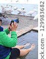 Chinese tourists take photos of swans on their smartphones while warming their feet in the sand baths at Lake Kussharo 129983682