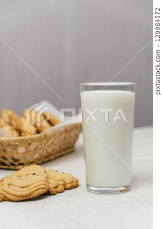 milk and cookies on table with basket of baked treats in background during cozy snack time. closeup. 129984572