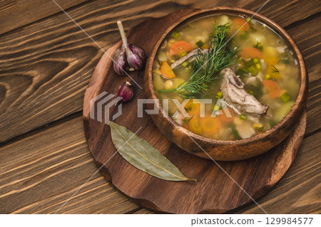 delicious homemade pea soup served in wooden bowl garlic and herbs on rustic wooden table. closeup. delicious homemade pea soup served in wooden bowl garlic and herbs on rustic wooden table. closeup. 129984577
