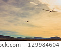 A single-engine aircraft tows a glider against the backdrop of mountains at sunset. 129984604