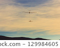 A single-engine aircraft tows a glider against the backdrop of mountains at sunset. 129984605