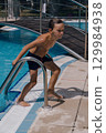 A boy is standing on a pool ladder and splashing water 129984938