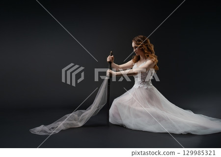 Elegant bride holding a sword in a dreamy lingerie-inspired setting 129985321