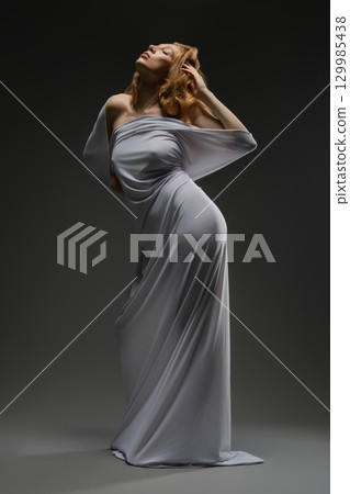 Sensual pose of a woman in lingerie with a flowing fabric draped around her 129985438