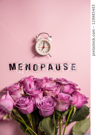 Word Menopause with pink roses and alarm clock, flat lay, pink background 129985483