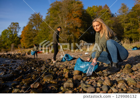 Focused young woman in environment conservation team picking up plastic at beach 129986132