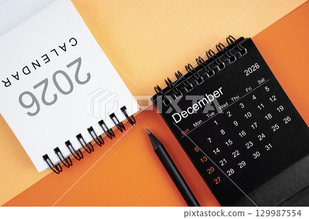 December 2026 desk calendar black and white color with pencil on orange color background. 129987554