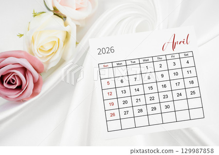 April 2026 calendar page and rose flower on white satin textile background. April 2026 calendar page and rose flower on white satin textile background. 129987858