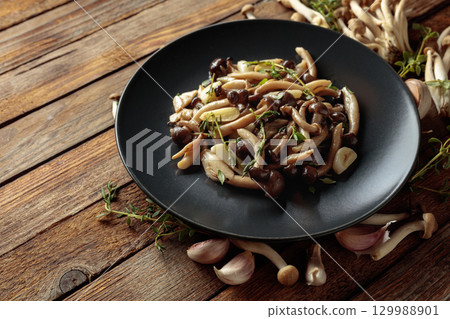 Fried shimeji mushrooms with thyme and garlic on a black plate. 129988901