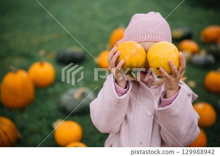 A child holds two yellow pumpkins while surrounded by various pumpkins at a farm in autumn A child holds two yellow pumpkins while surrounded by various pumpkins at a farm in autumn 129988942