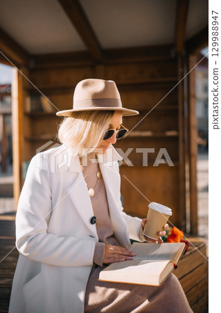 Woman enjoying coffee while reading in a cozy outdoor space in the city Woman enjoying coffee while reading in a cozy outdoor space in the city 129988947