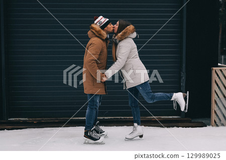 Couple enjoying ice skating together while sharing a romantic kiss in a winter setting Couple enjoying ice skating together while sharing a romantic kiss in a winter setting 129989025