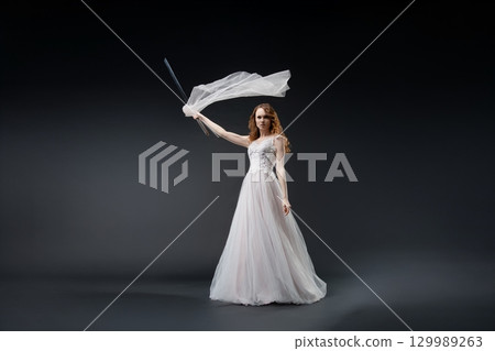 Elegant bride in stunning lingerie-inspired dress holding a flowing veil 129989263