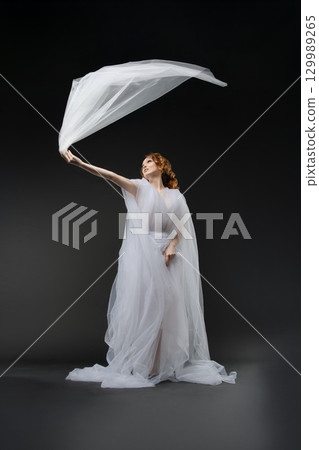 Elegant bride in sheer lingerie embracing a flowing veil in dramatic light Elegant bride in sheer lingerie embracing a flowing veil in dramatic light 129989265
