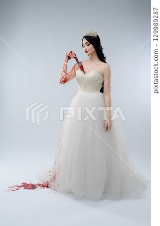 Beauty in white gown challenges darkness with bloody knife 129989287