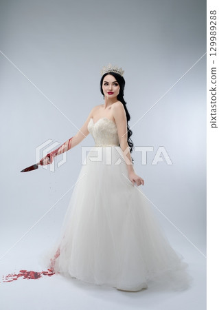Bridal beauty in white gown holds knife with blood for dramatic effect 129989288