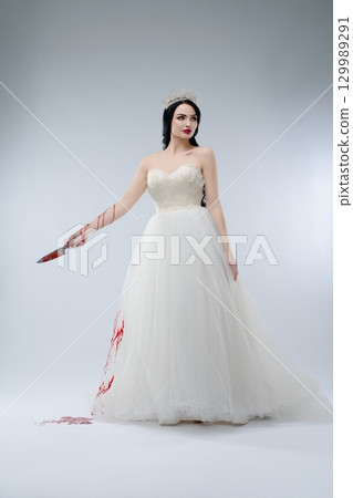 Bride in white gown holding a bloodied knife in a haunting portrayal of elegance Bride in white gown holding a bloodied knife in a haunting portrayal of elegance 129989291