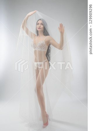 Beautiful bride in delicate lingerie poses with soft veil 129989296