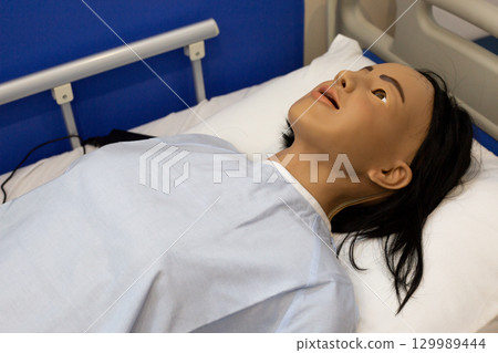 Realistic medical mannequin lying in hospital bed for healthcare training, clinical simulation and nursing practice. Used to teach patient assessment monitoring, airway skills. Emergency response 129989444