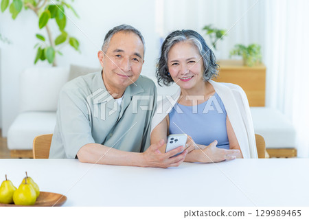 一對老夫婦在客廳裡看智能手機 129989465