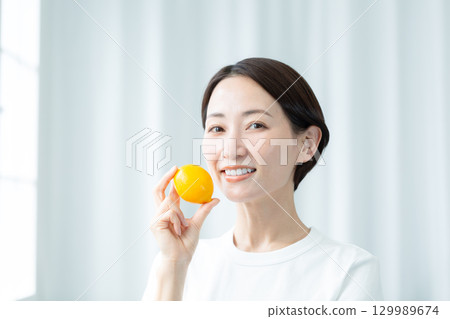一位面容清秀的女士手捧檸檬，露出清新的笑容。特寫照片。 129989674