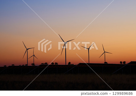 Silhouetted wind turbines and solar panels at sunset Silhouetted wind turbines and solar panels at sunset 129989686